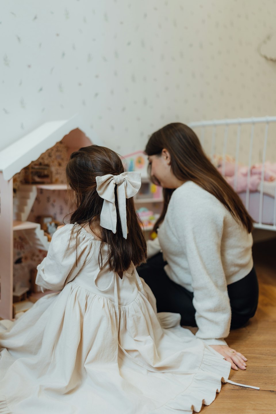 An adult and child play with a small dollhouse.